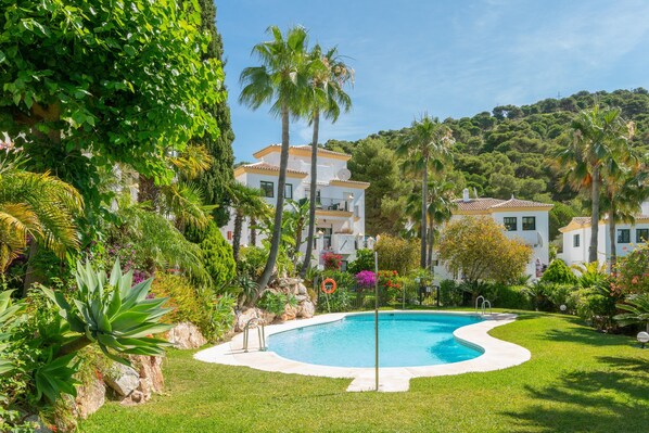 Piscina cercada por vegetação exuberante e edifícios brancos com varandas.