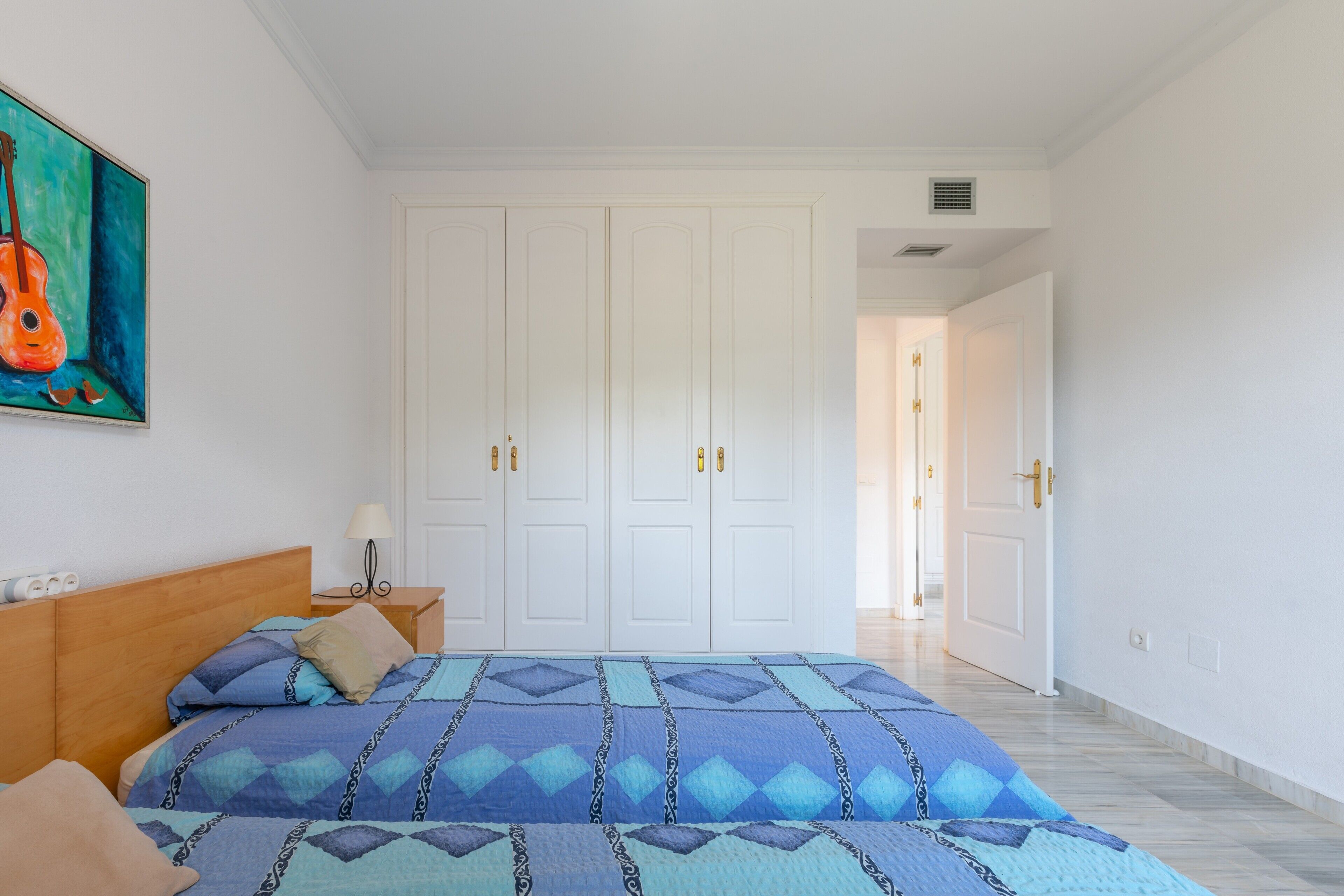 Een slaapkamer met een bed, nachtkastje, lamp, schilderij en een kledingkast.