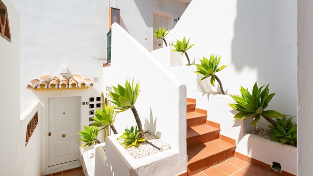 A white building with a white door, a staircase, and potted plants.