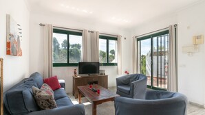 A living room with a sofa, armchairs, a coffee table, a TV, and a balcony with a view.