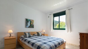 A bedroom with a bed, two bedside tables, a nightstand, a window with curtains, and a painting on the wall.