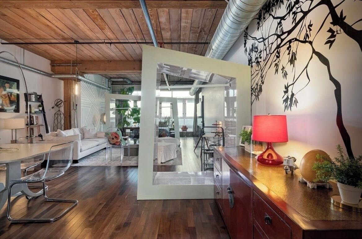 Un intérieur moderne avec un plafond en bois, un coin repas séparé par une cloison en verre transparent, une lampe rouge et une fresque murale.