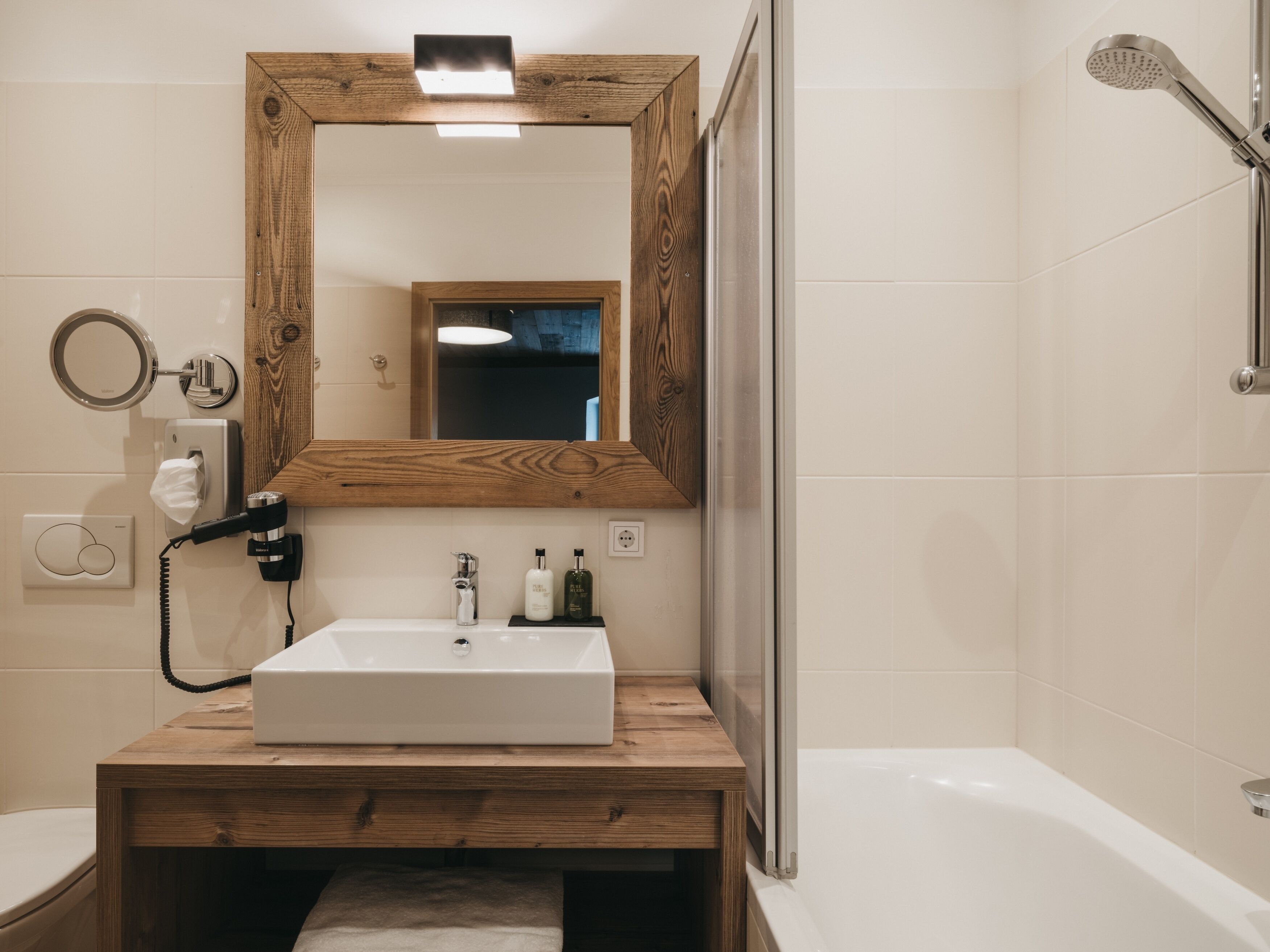 Un baño con tocador de madera, un espejo grande, un lavamanos, una toalla, un inodoro y una ducha.