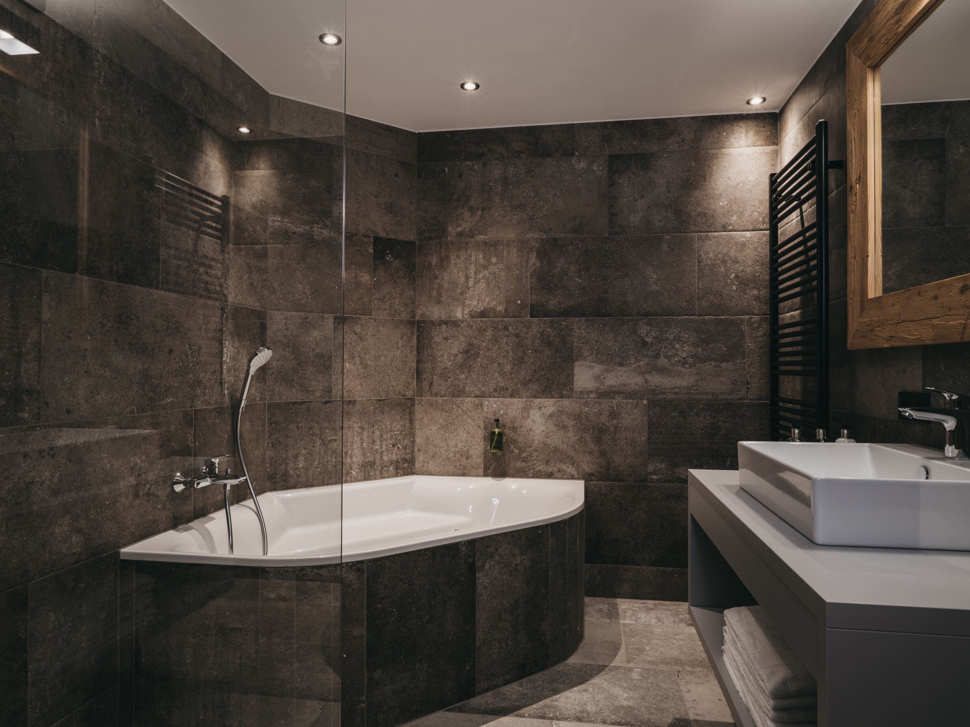 A modern bathroom with a freestanding bathtub, a vanity with a mirror, and dark stone walls.