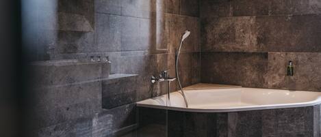 Un baño moderno con una bañera independiente, un cabezal de ducha y un estante pequeño.