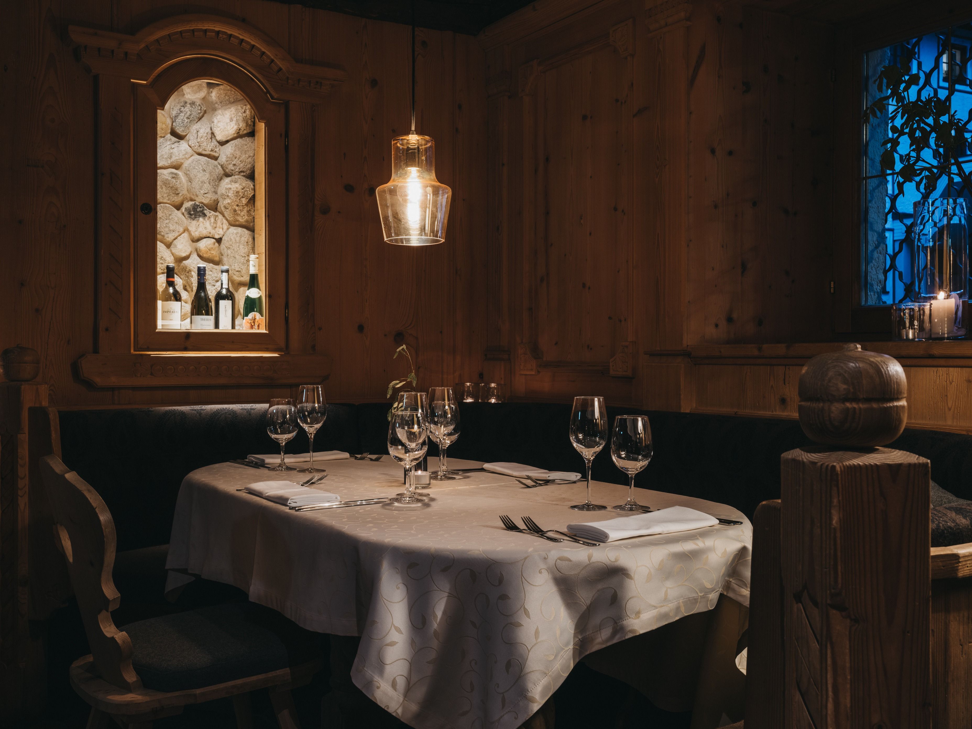 A dining area with a round table set for two, a stone-framed window, and a wooden wall.