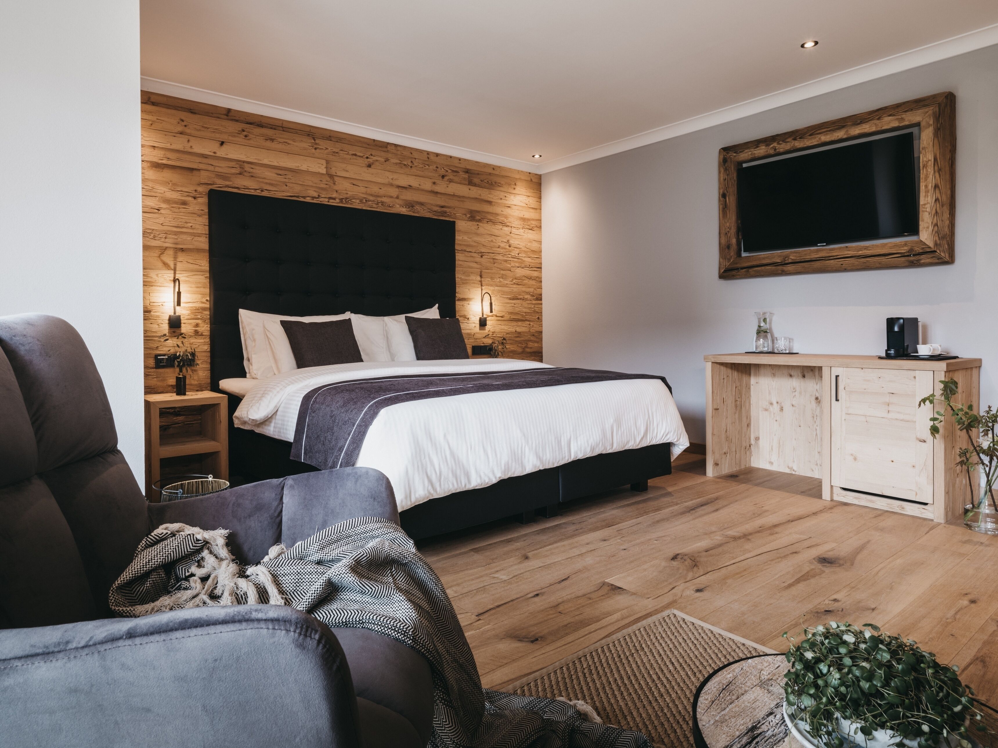 Een moderne slaapkamer met een houten hoofdbord, een groot bed, een nachtkastje met lamp, een houten kast en een aan de muur bevestigde televisie.