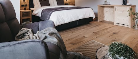 A modern bedroom with a wooden headboard, a large bed, a bedside table with a lamp, a wooden cabinet, and a television mounted on the wall.