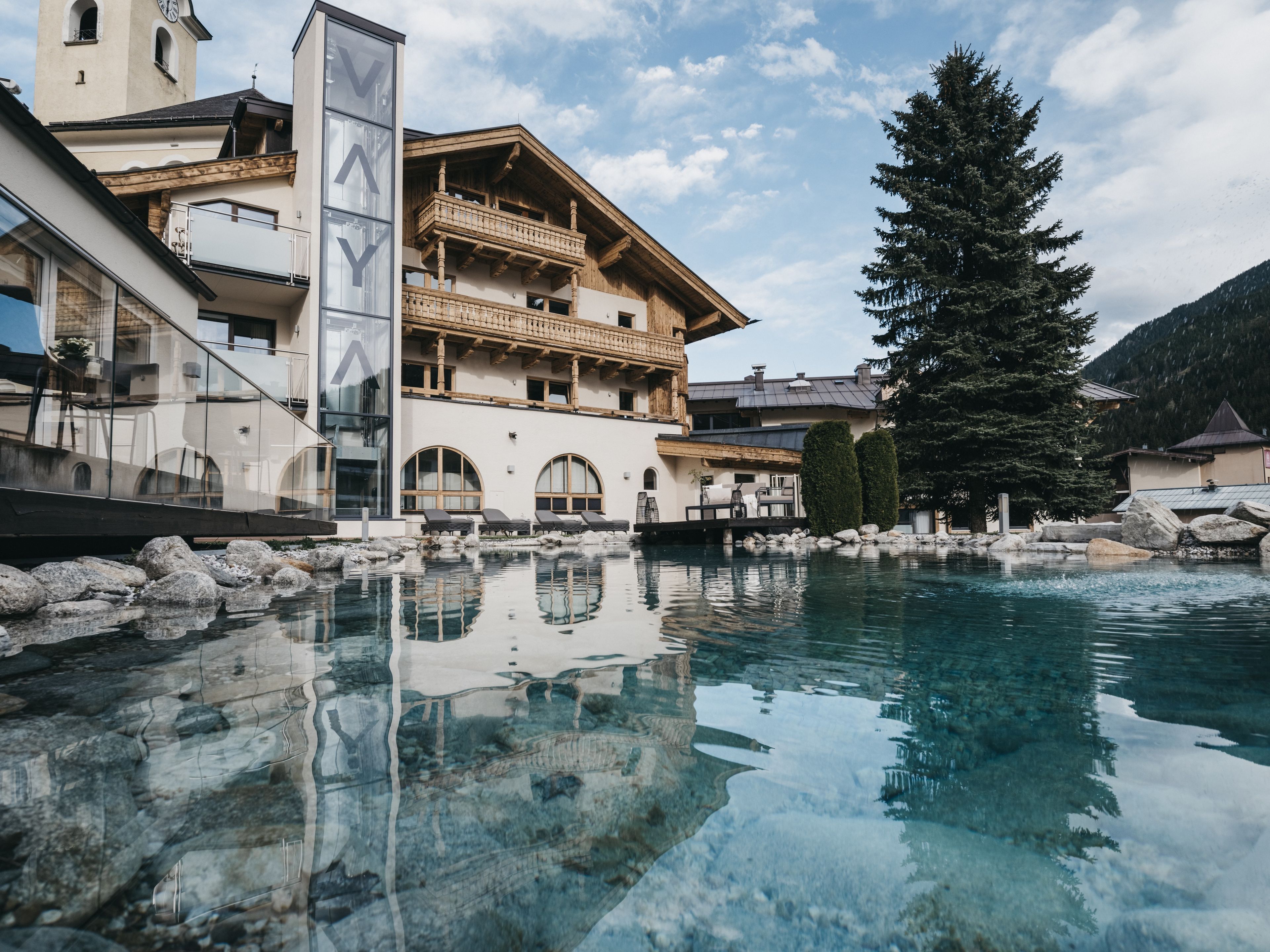 A hotel with a pool, wooden balconies, and a mountain backdrop.