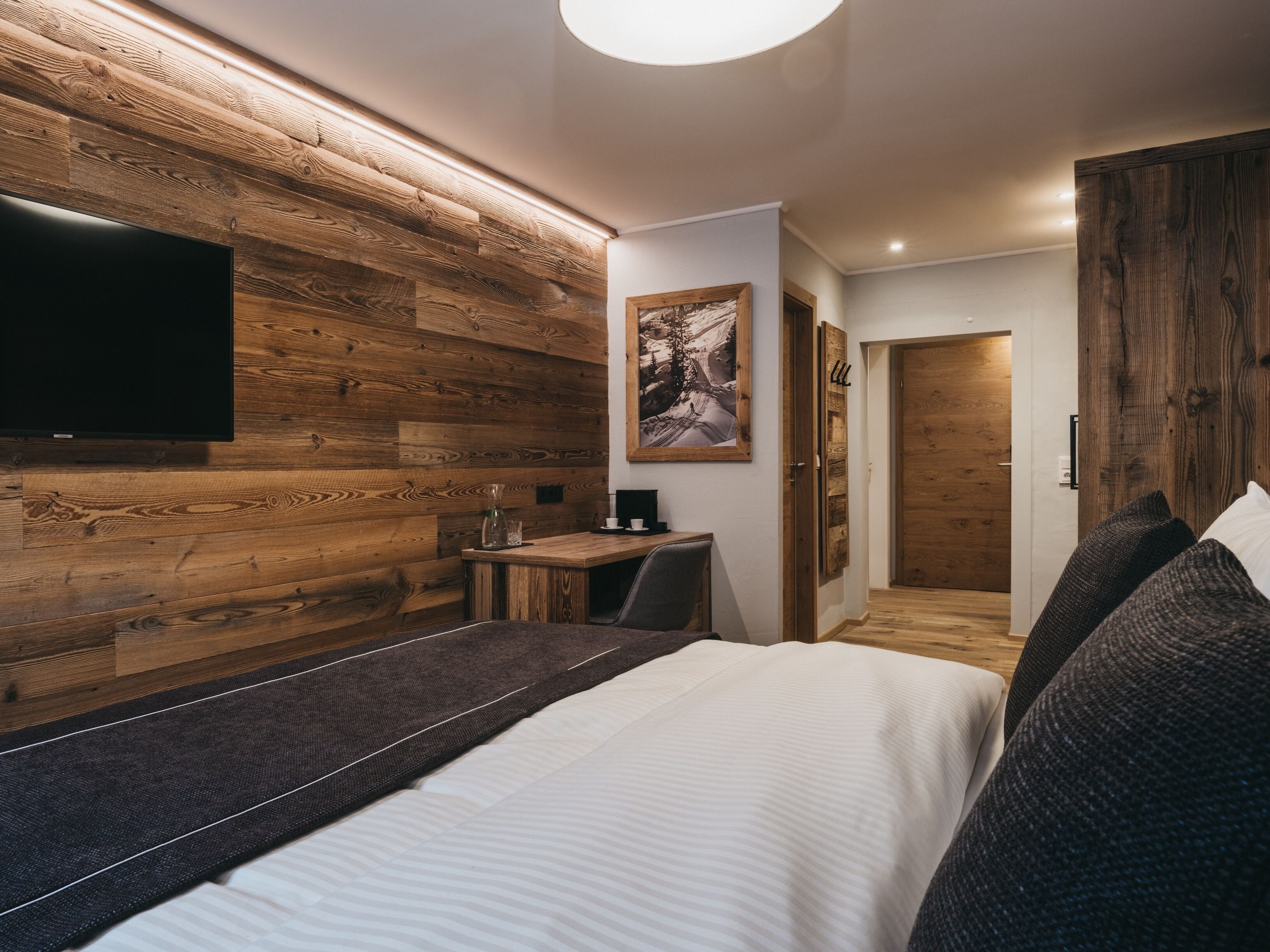 Une chambre moderne avec un mur en bois, un téléviseur à écran plat, un bureau et un lit avec des oreillers.