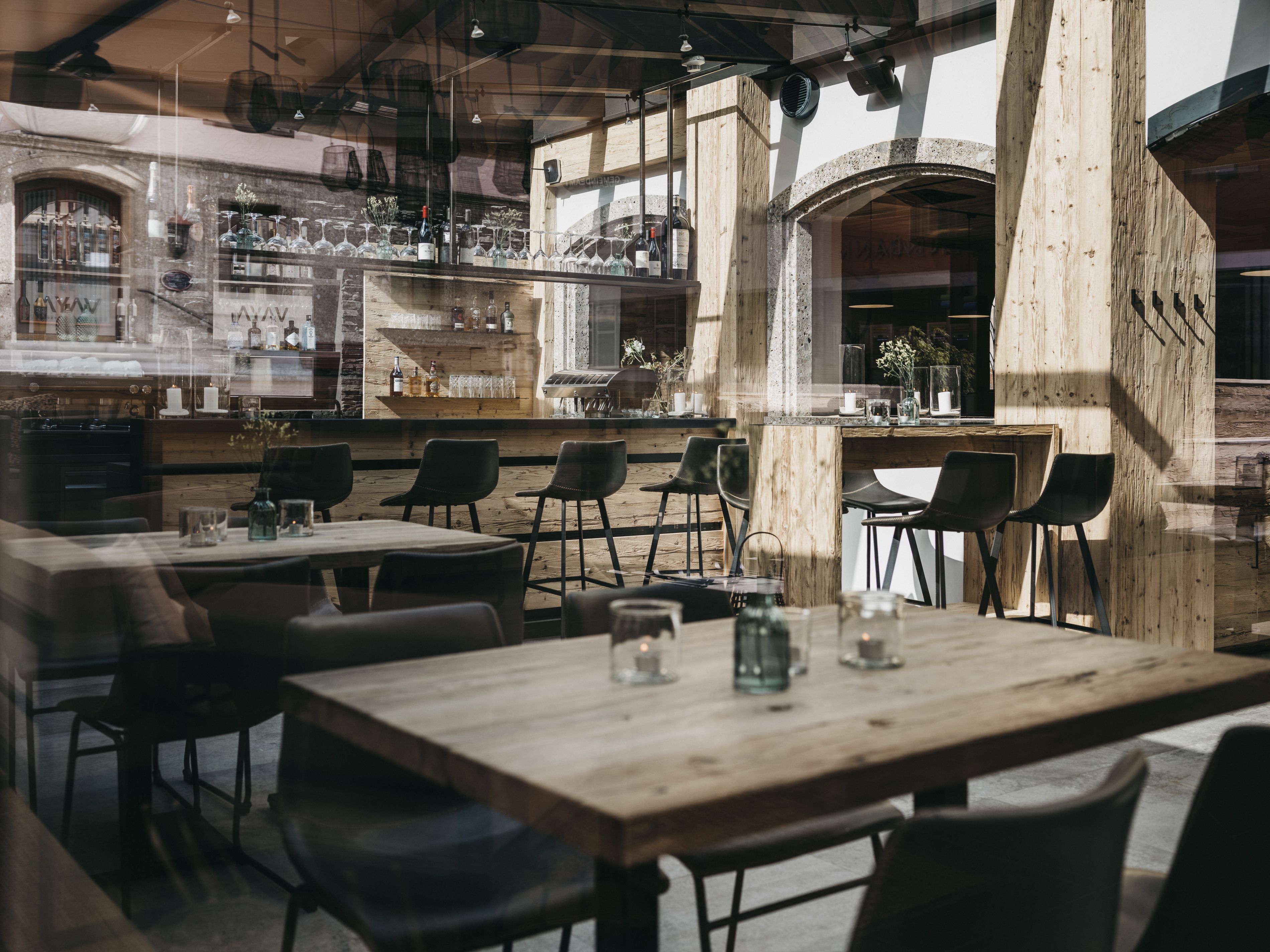 A restaurant interior with wooden tables and chairs, a bar area with bottles and glasses, and a view through a window.