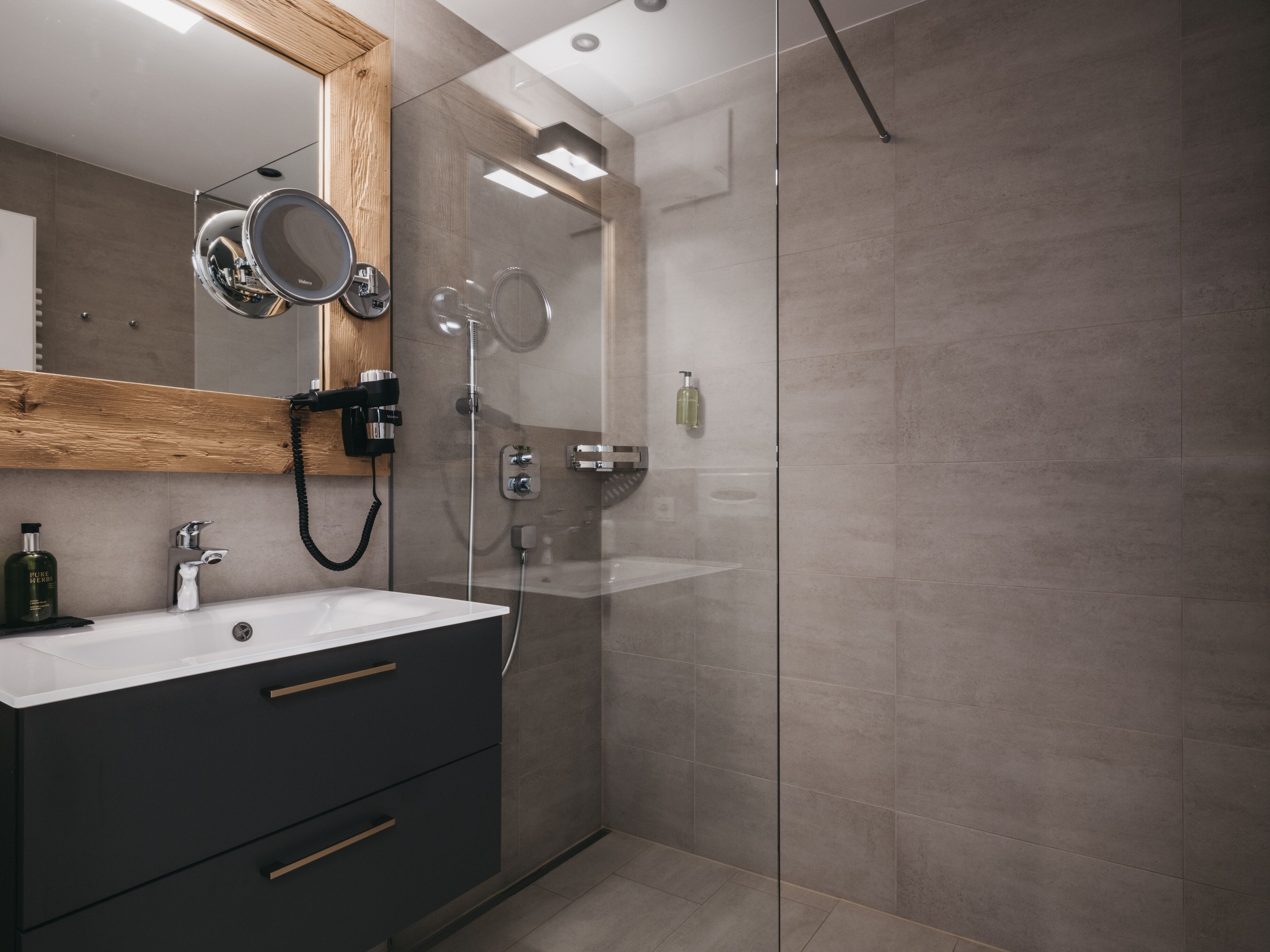 A modern bathroom with a glass shower enclosure, a vanity with a mirror, and a wooden shelf.