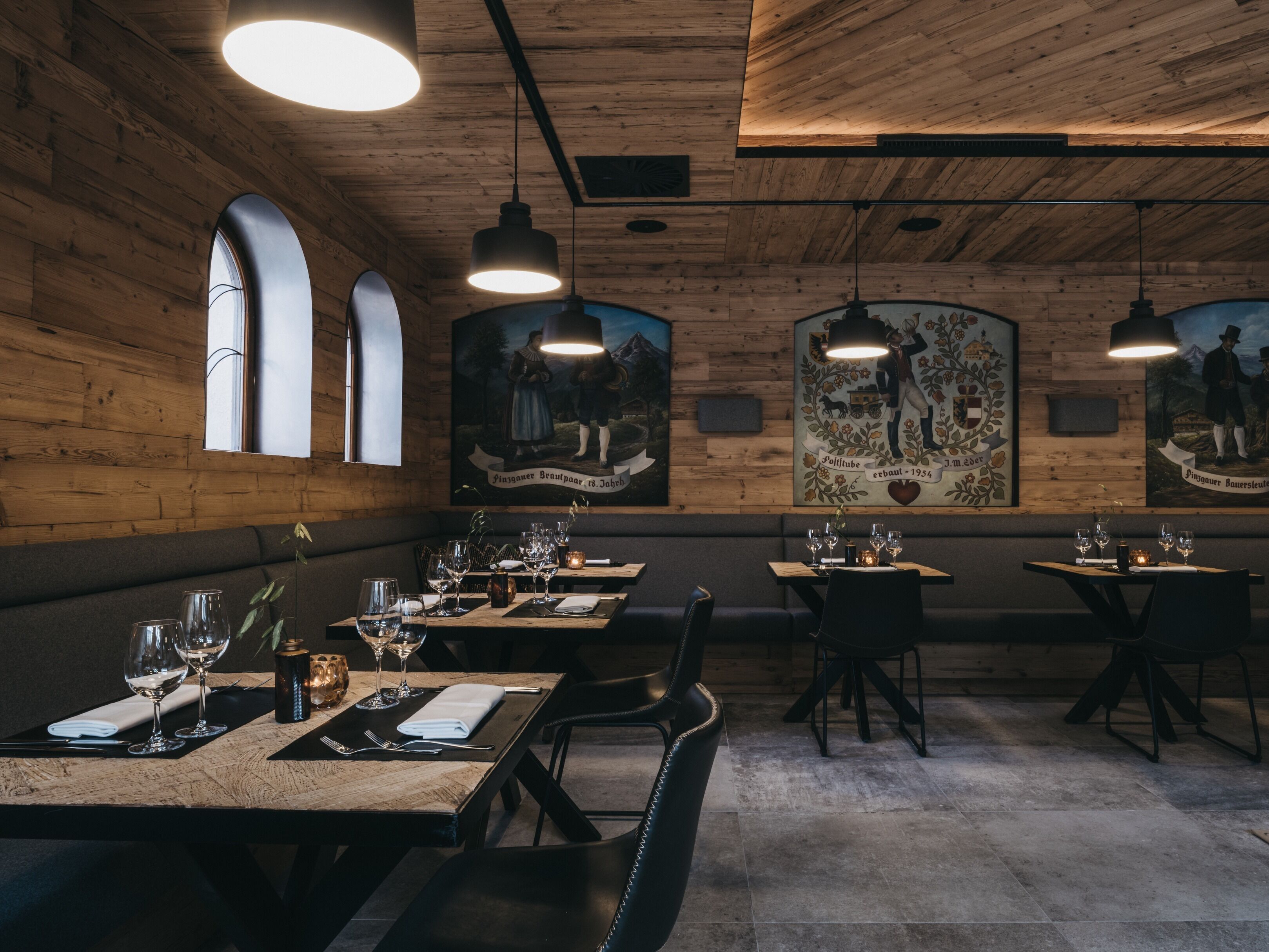 A restaurant with wooden walls and ceiling, featuring tables set with wine glasses and plates, and artwork on the walls.