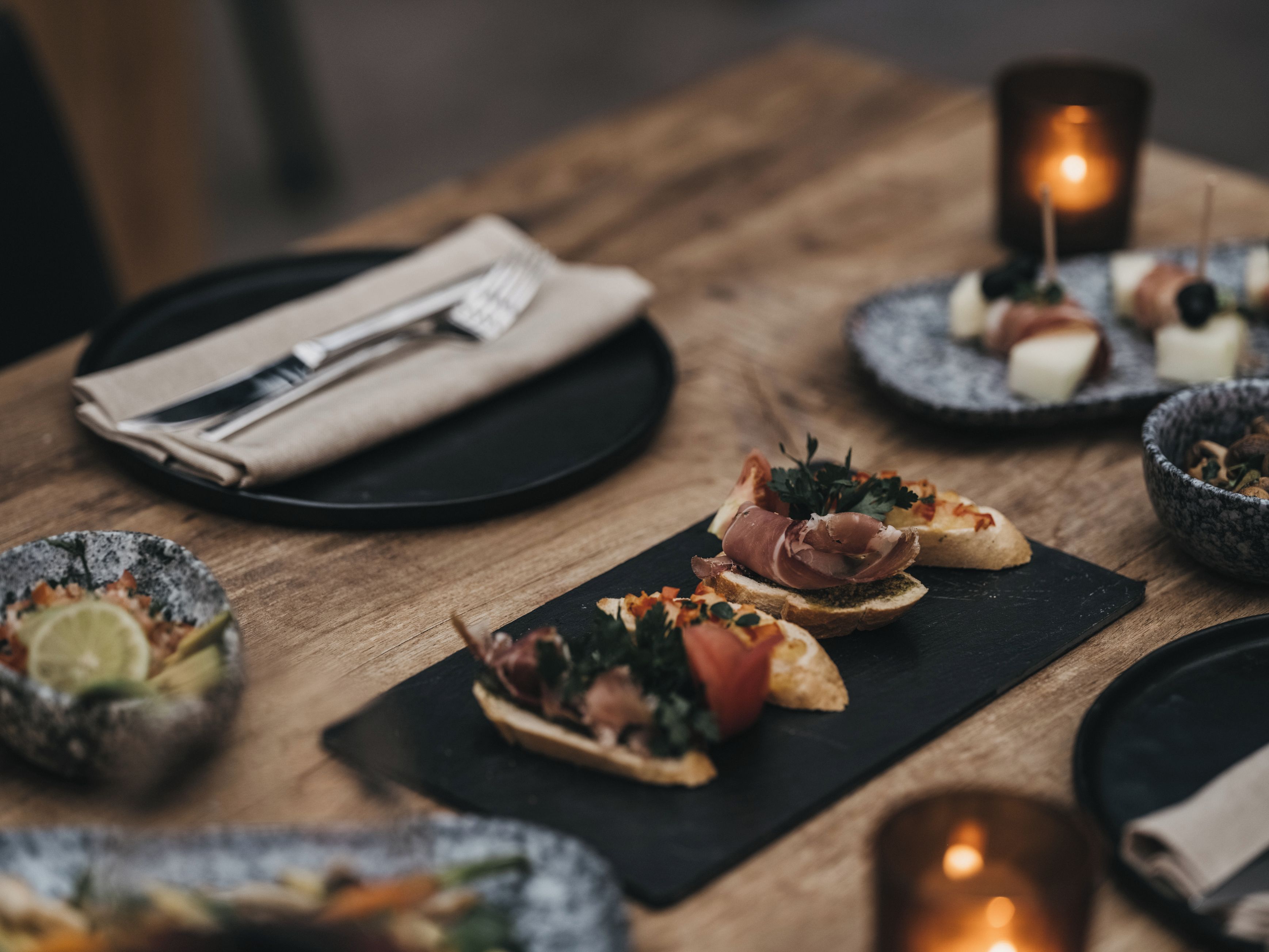 Una mesa de comedor con platos de comida, una servilleta, cubiertos y velas.
