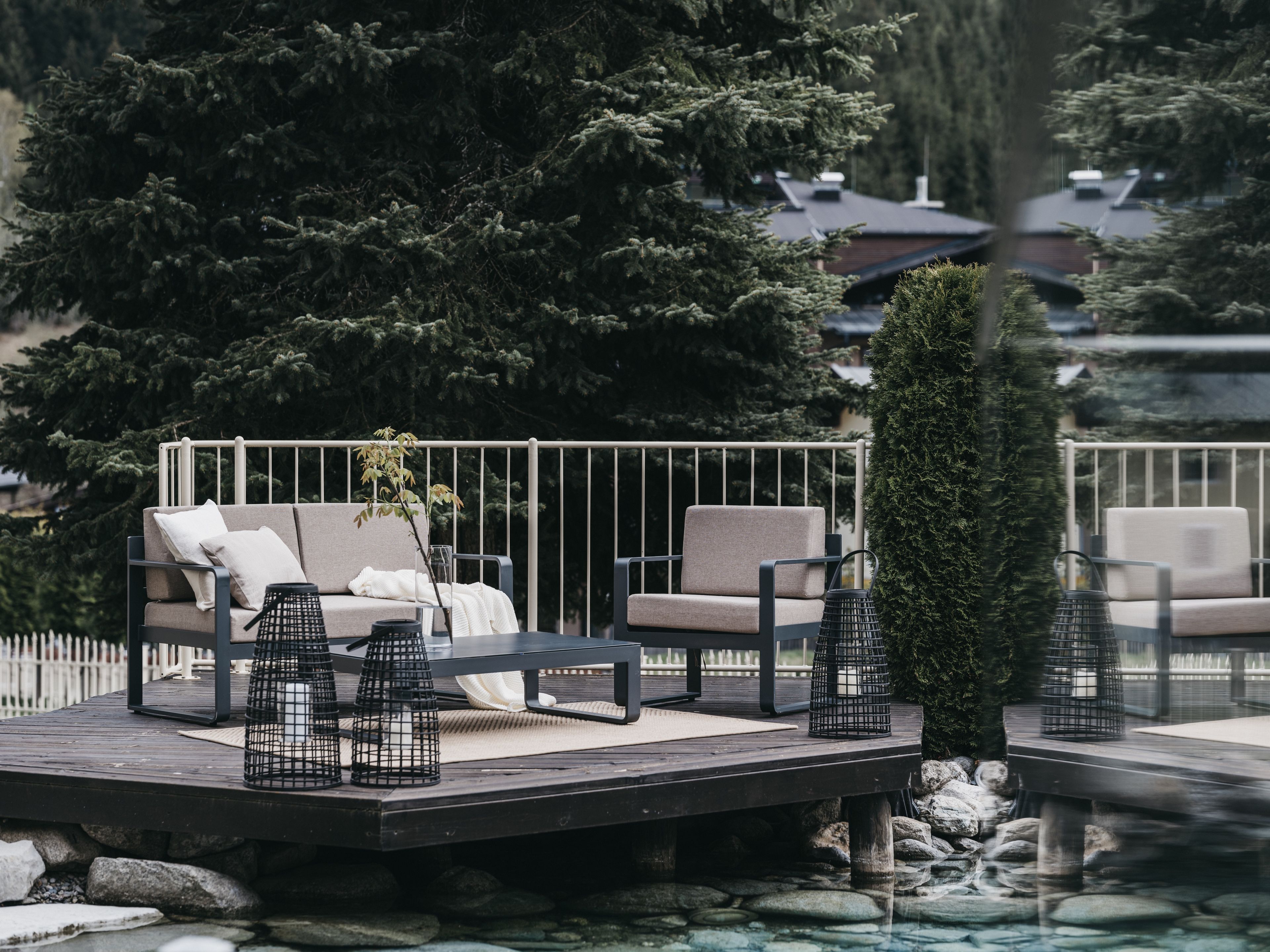 A deck with a sofa and chairs, surrounded by trees and a body of water.