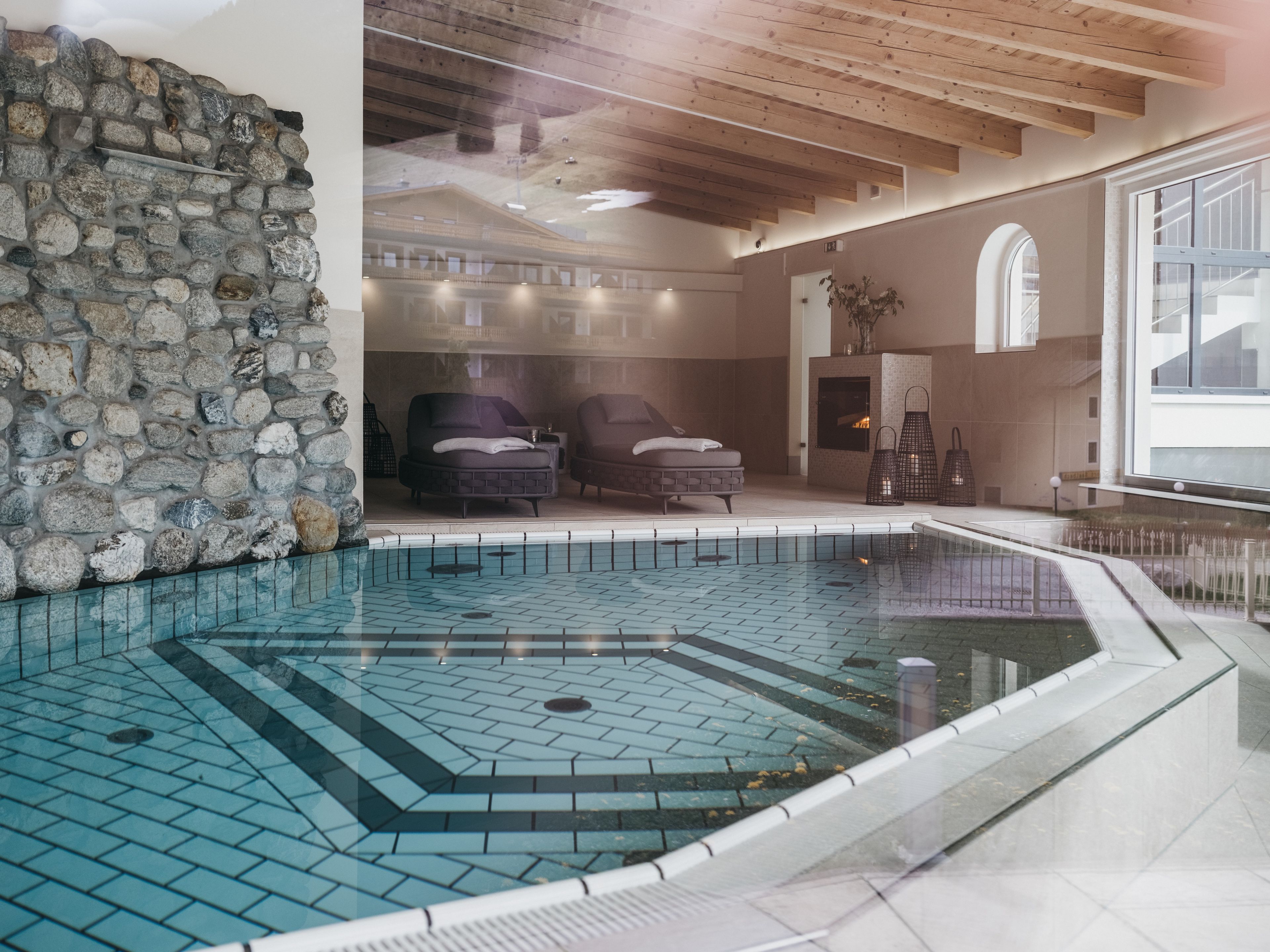 Una piscina con un muro de piedra, dos sillas de descanso y techo de madera.