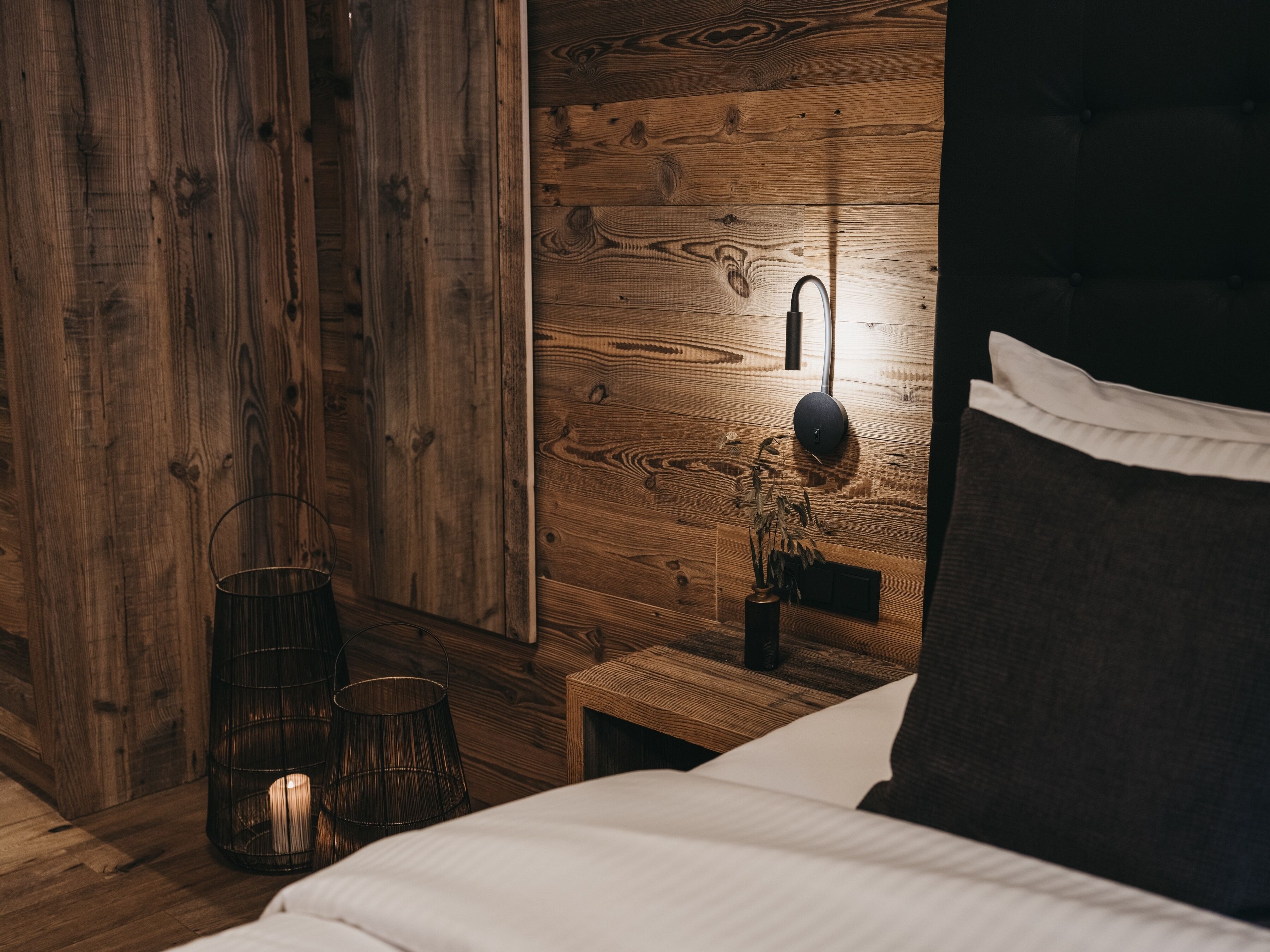 Een slaapkamer met een houten hoofdbord, een nachtkastje met een lamp en een wandlamp.