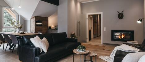 A modern living room with a black leather sofa, a dining area with a wooden table, and a fireplace.
