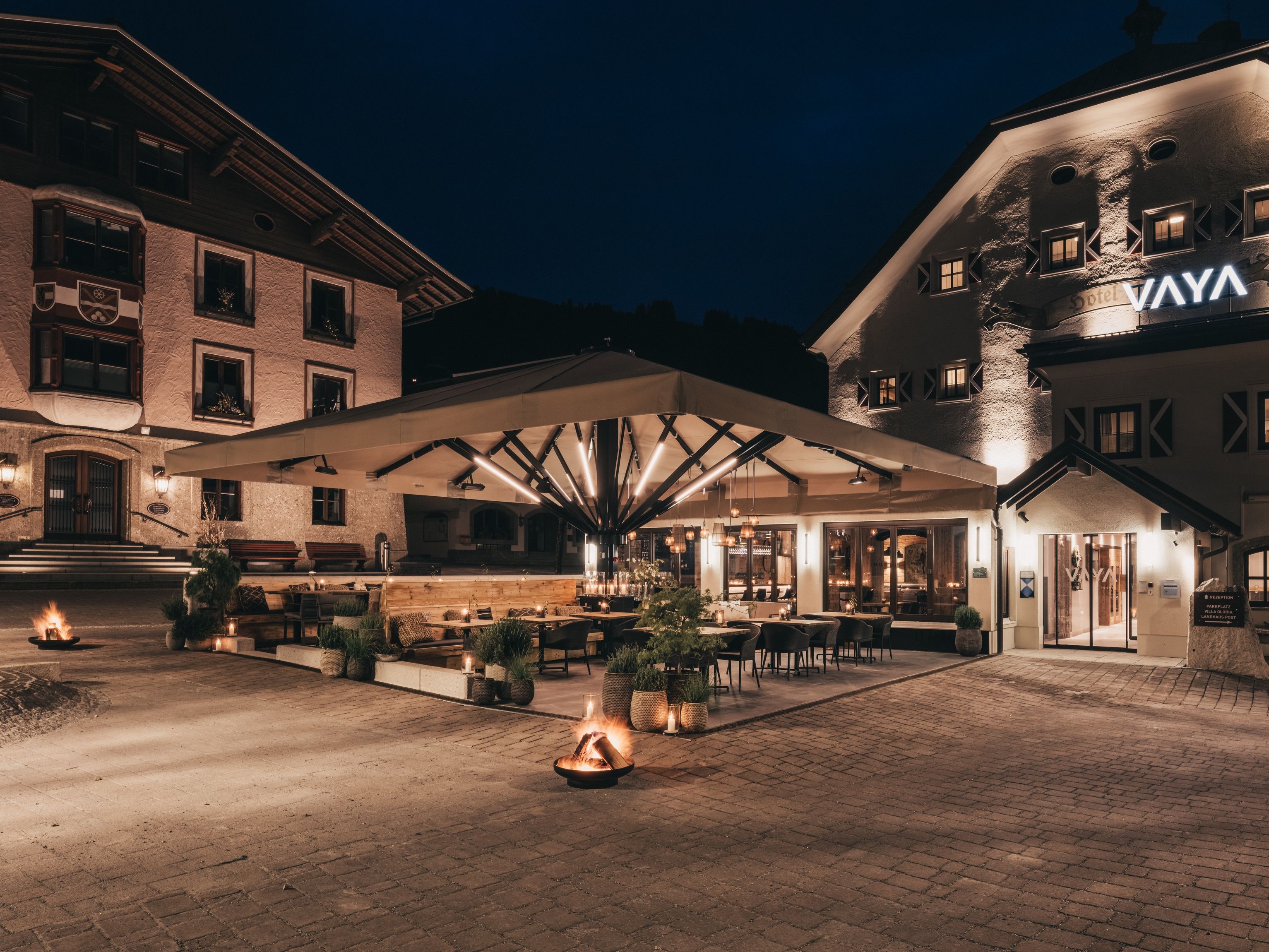 Een hotel binnenplaats met terras, een receptie en een gebouw met een bord waarop 'VAYA' staat.