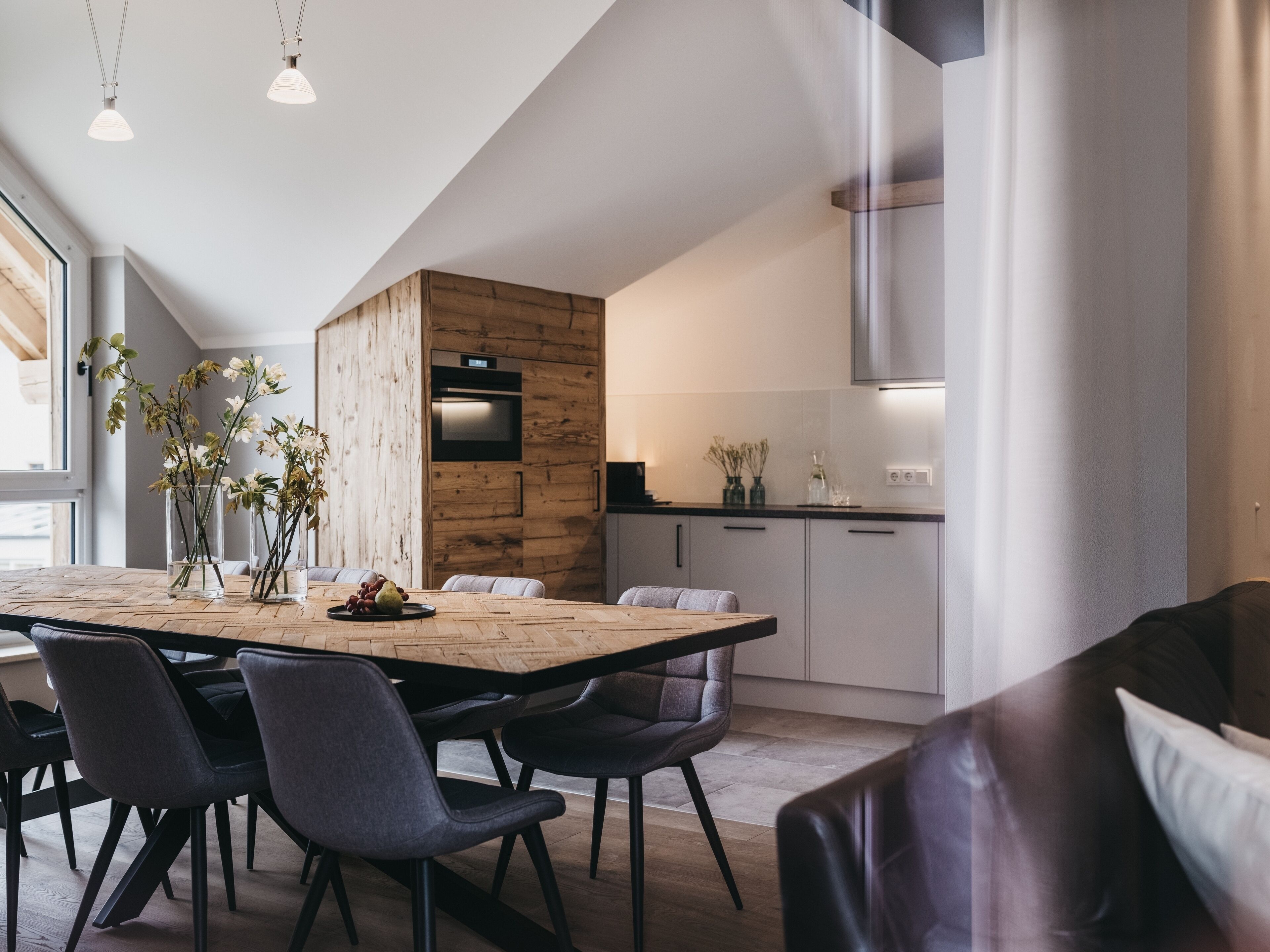 A modern kitchen with a wooden accent wall, a dining area with a large table and chairs, and pendant lighting.