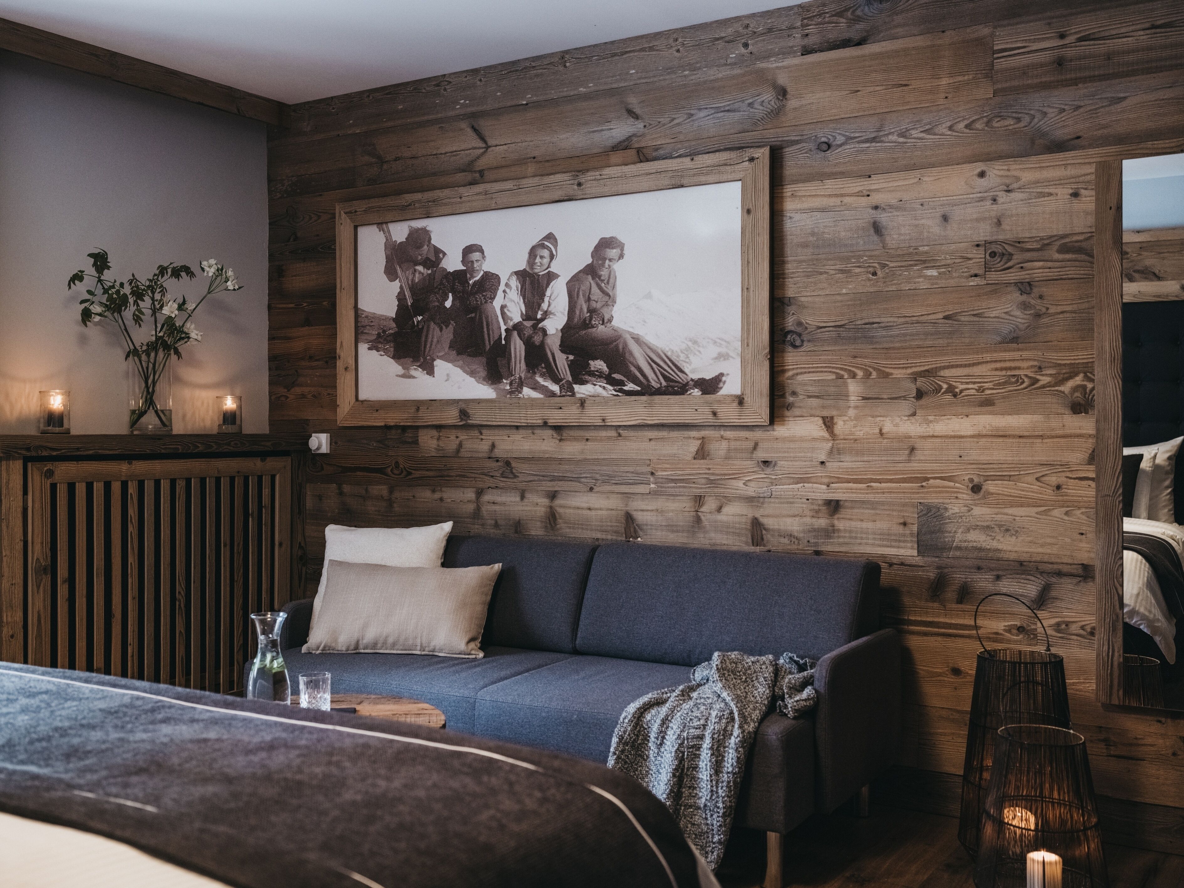 A cozy room with a wooden wall, a framed black and white photo, a blue sofa, and a vase with flowers.