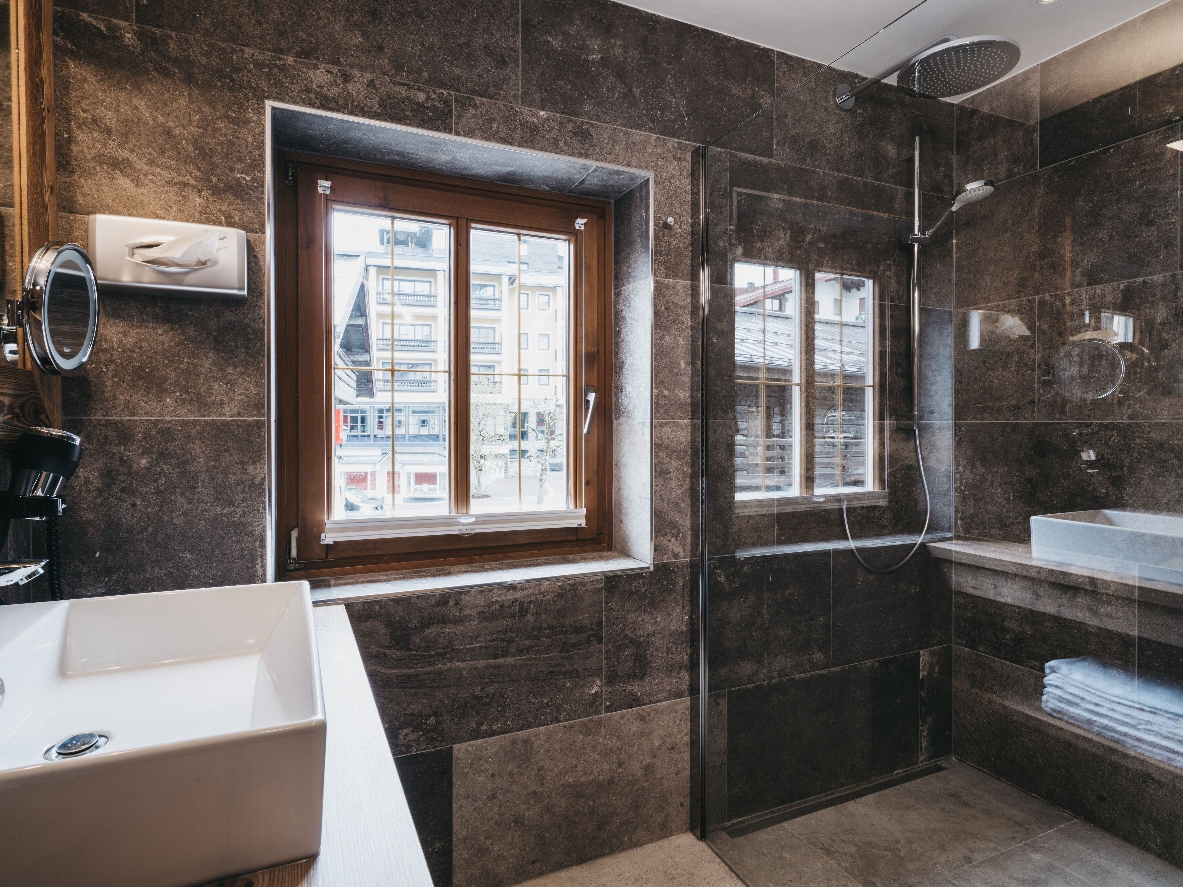 A modern bathroom with a large window, a glass shower enclosure, and a white sink.