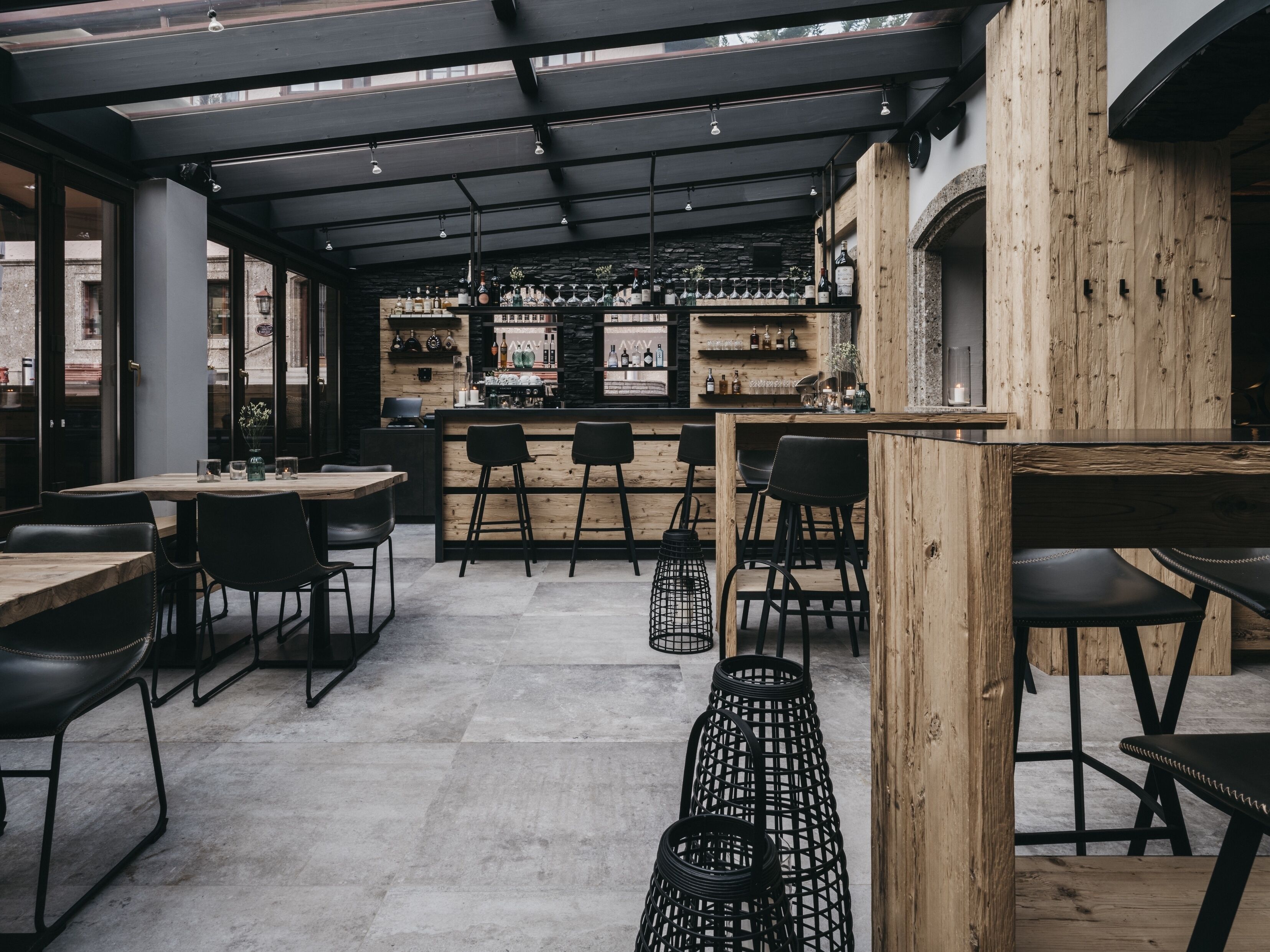 Un espace bar moderne agrémenté d’éléments en bois, de tabourets et d’une variété de bouteilles et de verres exposés sur des étagères.