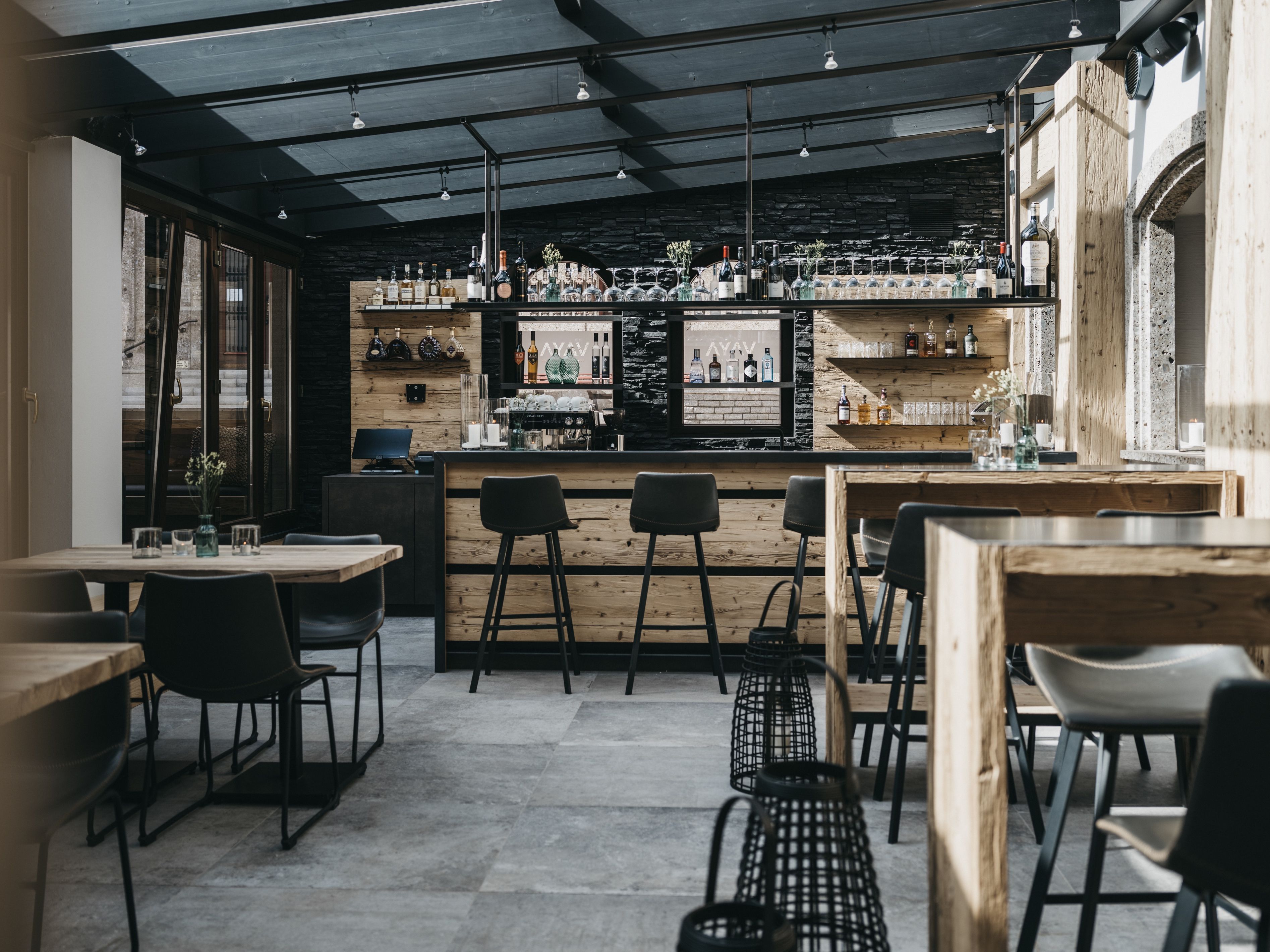 Zona de bar con mobiliario de madera, una barra con botellas y una pared de piedra.