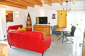 Ein modernes Wohnzimmer mit einem roten Ledersofa, einem Holzesstisch und einem Flachbildfernseher.