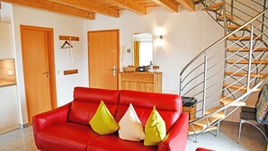 Un sofá de cuero rojo con tres cojines, una mesa de comedor de madera y una escalera de caracol.
