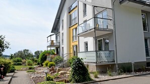 Un edificio residencial moderno de varios pisos con balcones, un camino pavimentado y un jardín ajardinado.
