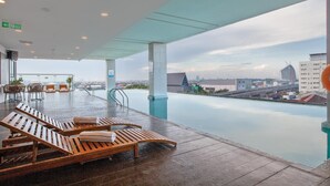 Ein Poolbereich auf dem Dach mit Liegestühlen und Blick auf die Stadt.