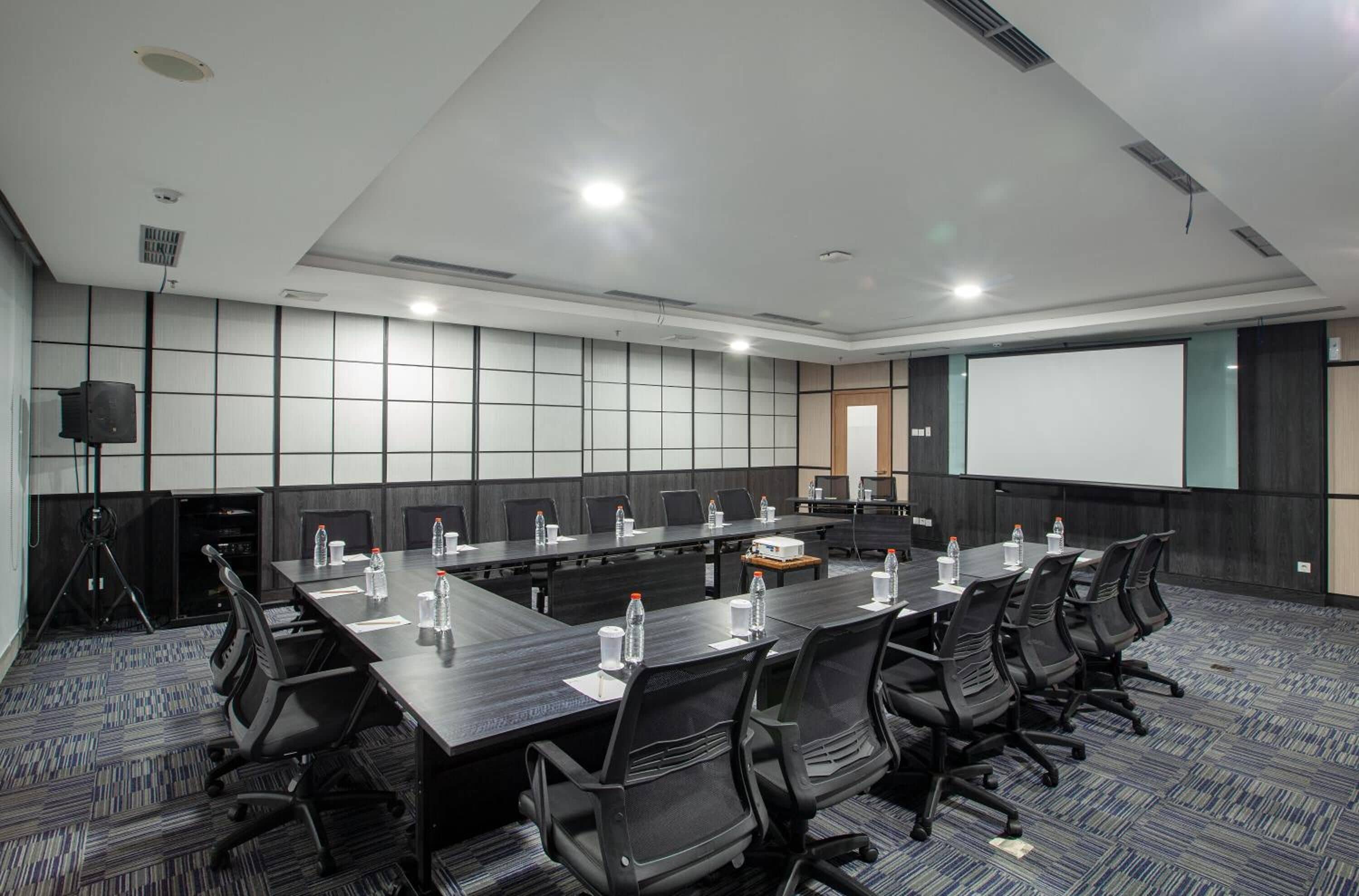 A conference room with a long table, chairs, a projector screen, and a whiteboard.