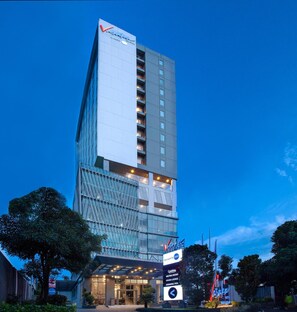 A tall hotel with a modern glass facade, a visible entrance, and a sign indicating amenities like meeting rooms and a swimming pool. - Vasaka Hotel Makassar Managed by Dafam (Makassar)