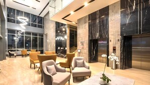 Eine moderne Lobby mit Marmorböden, zeitgenössischen Möbeln, einer digitalen Fahrstuhl-Anzeige und großen Fenstern.