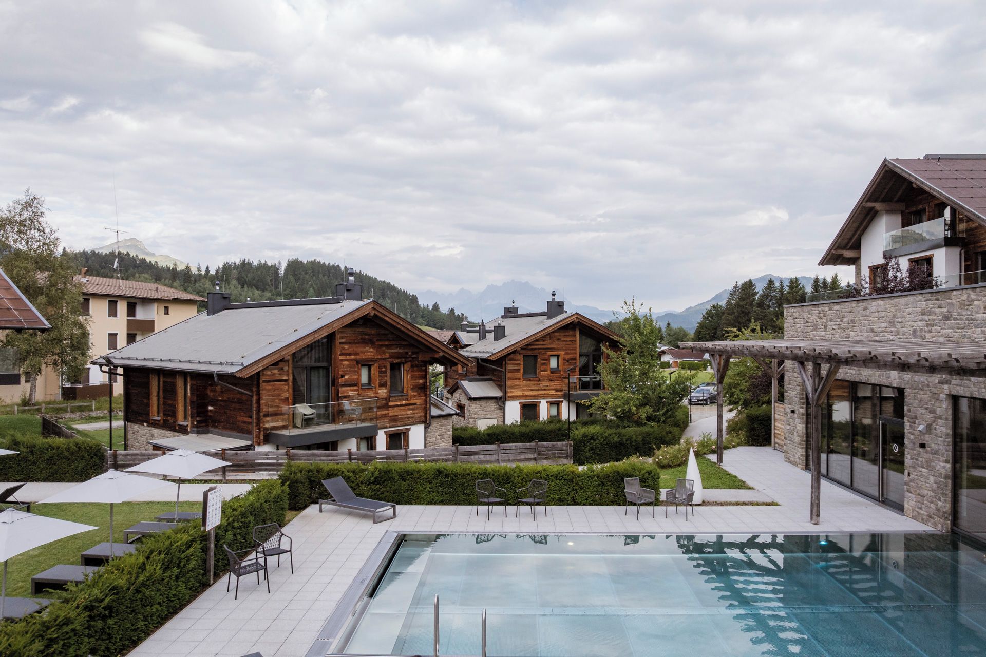A resort with wooden cabins, a swimming pool, and a mountainous backdrop.
