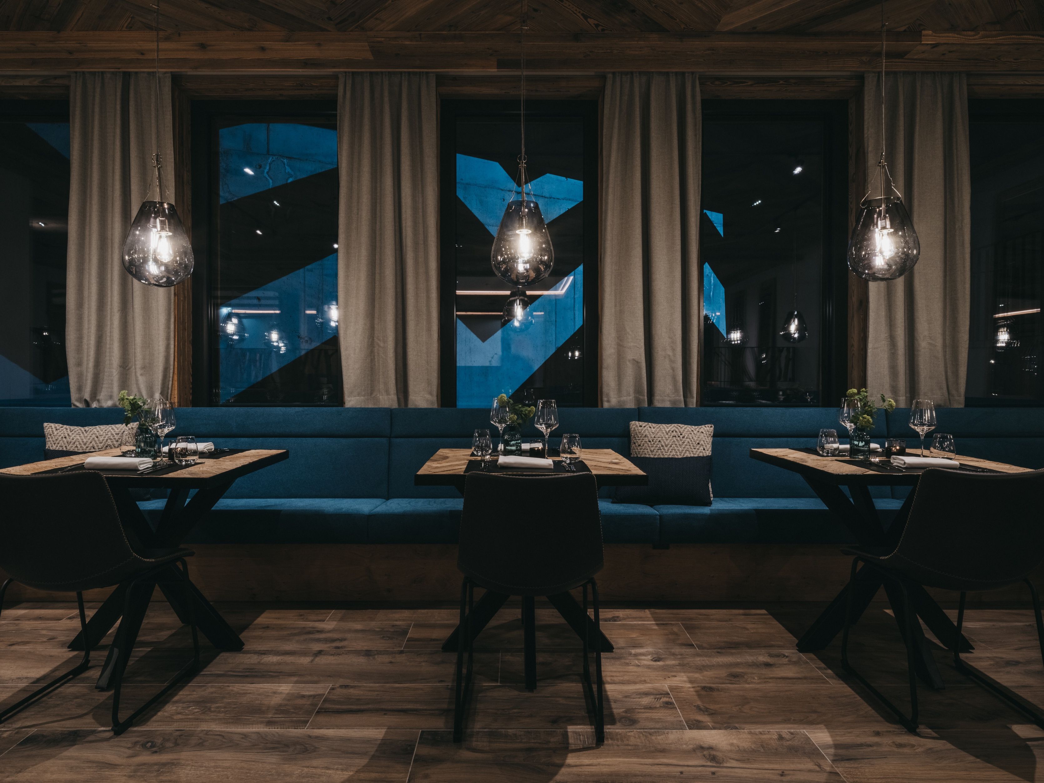 Un restaurante con sofá azul, mesas de madera y lámparas colgantes.