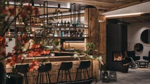 A bar area with wooden shelves, black chairs, and a fire feature. - VAYA Ladis (Ladis)