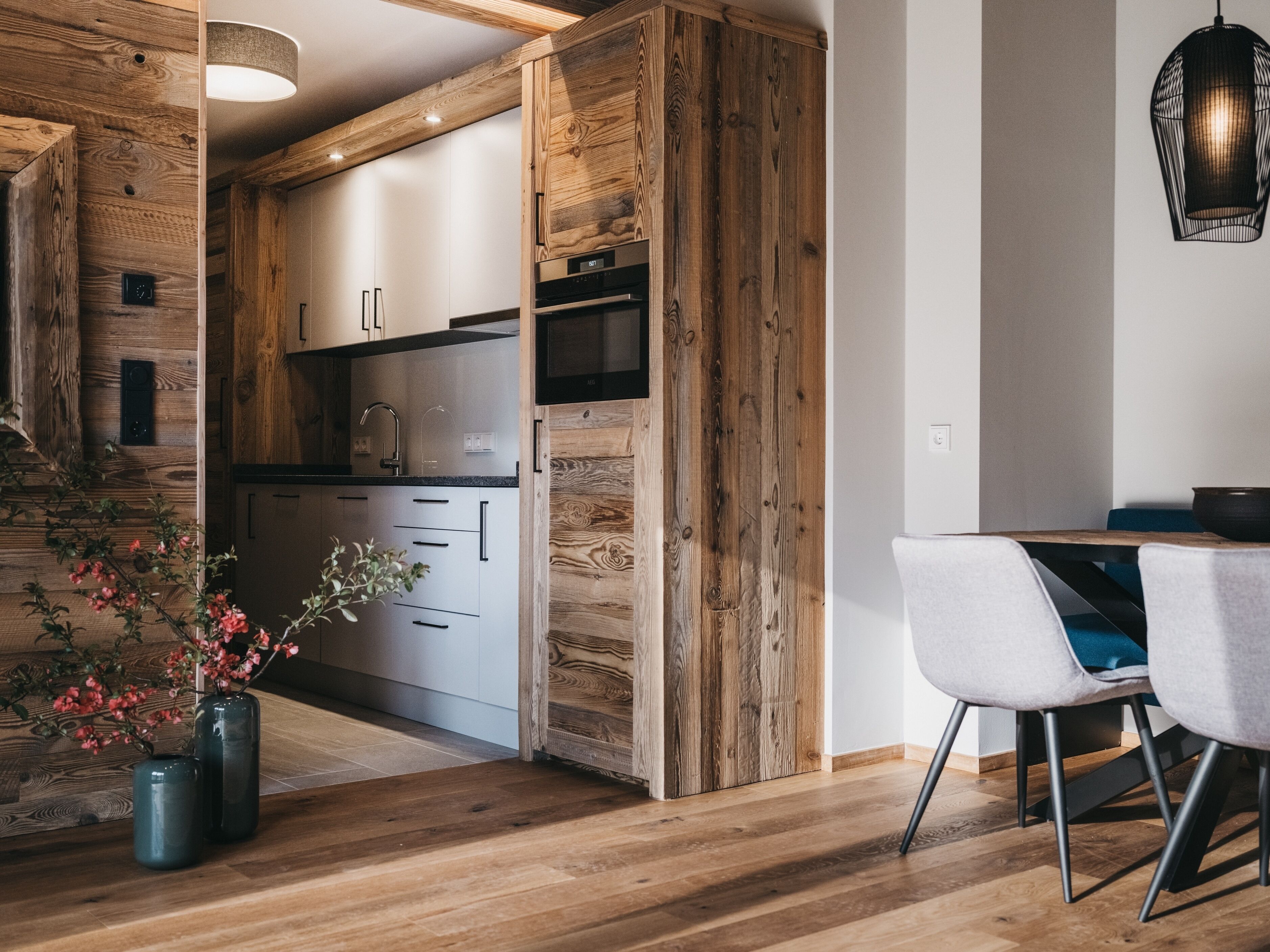 Una cocina moderna con detalles de madera, un comedor con mesa y sillas, y una lámpara colgante.