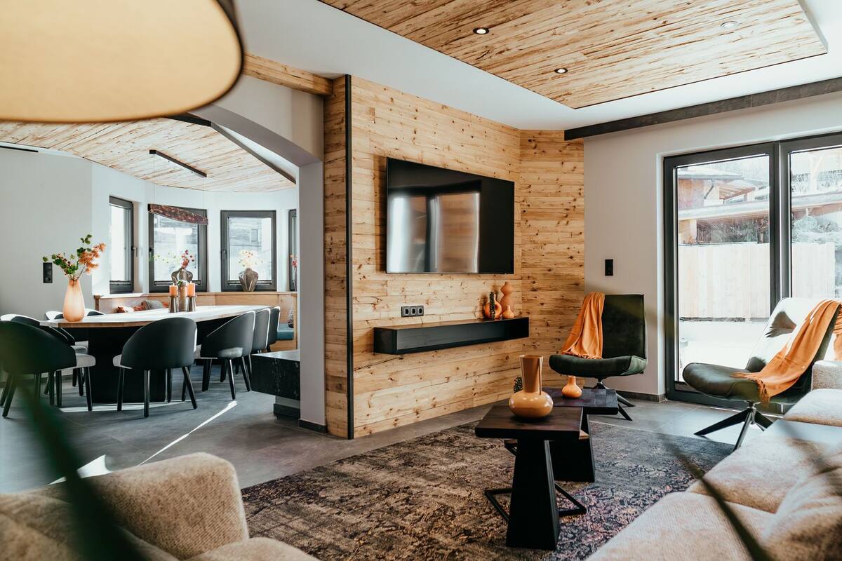 A modern living room with a wooden accent wall, a flat-screen TV, a fireplace, and a large window offering a view of the outdoors.