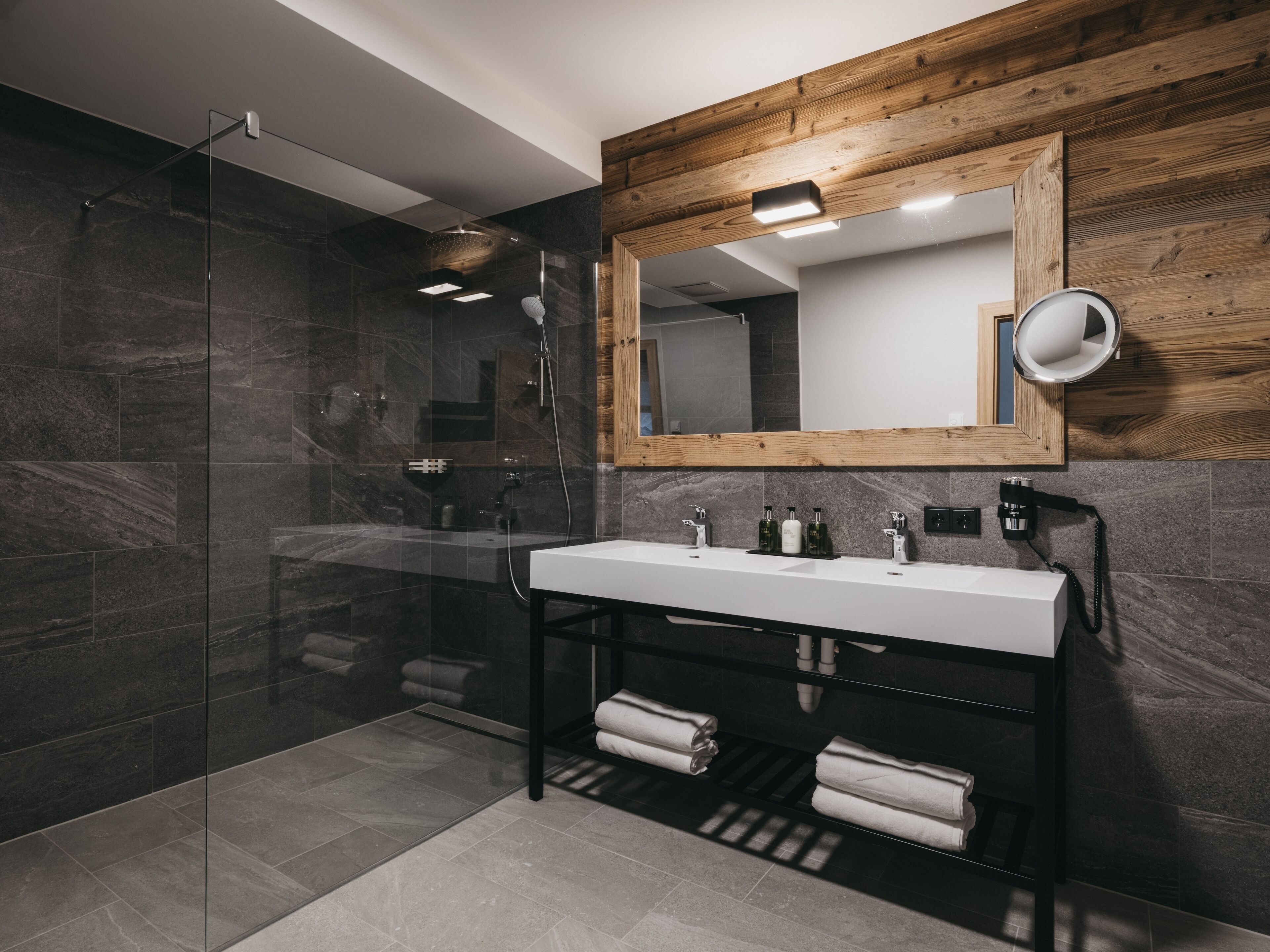 A modern bathroom with a glass shower enclosure, a wooden accent wall, and a large mirror above a white sink.