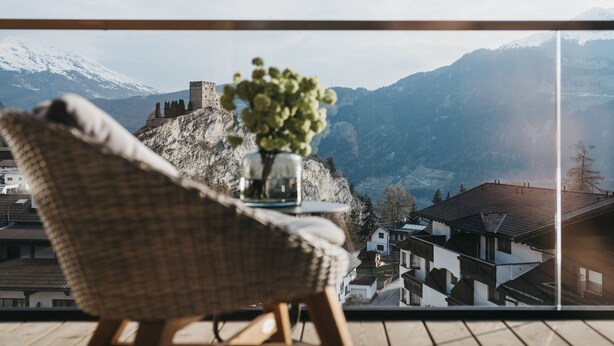 A wicker chair with a vase of flowers on a balcony overlooking a mountainous landscape with traditional buildings. - VAYA Ladis (Ladis)