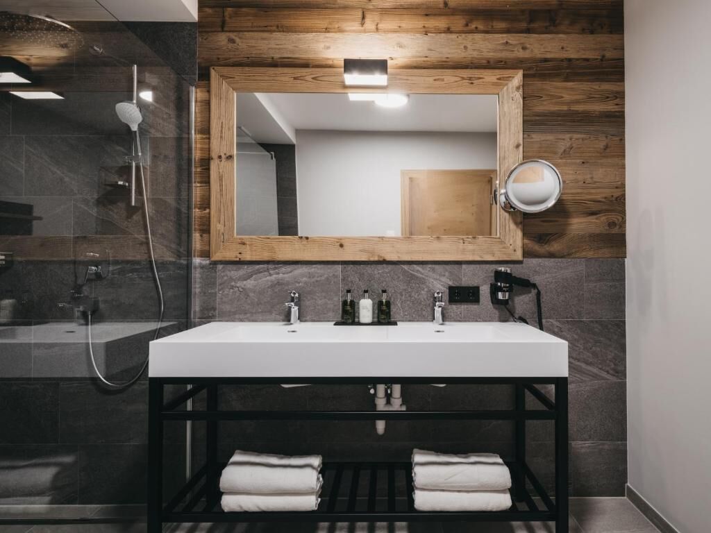 Une salle de bain moderne avec un grand miroir, un lavabo blanc et une douche à parois de verre.