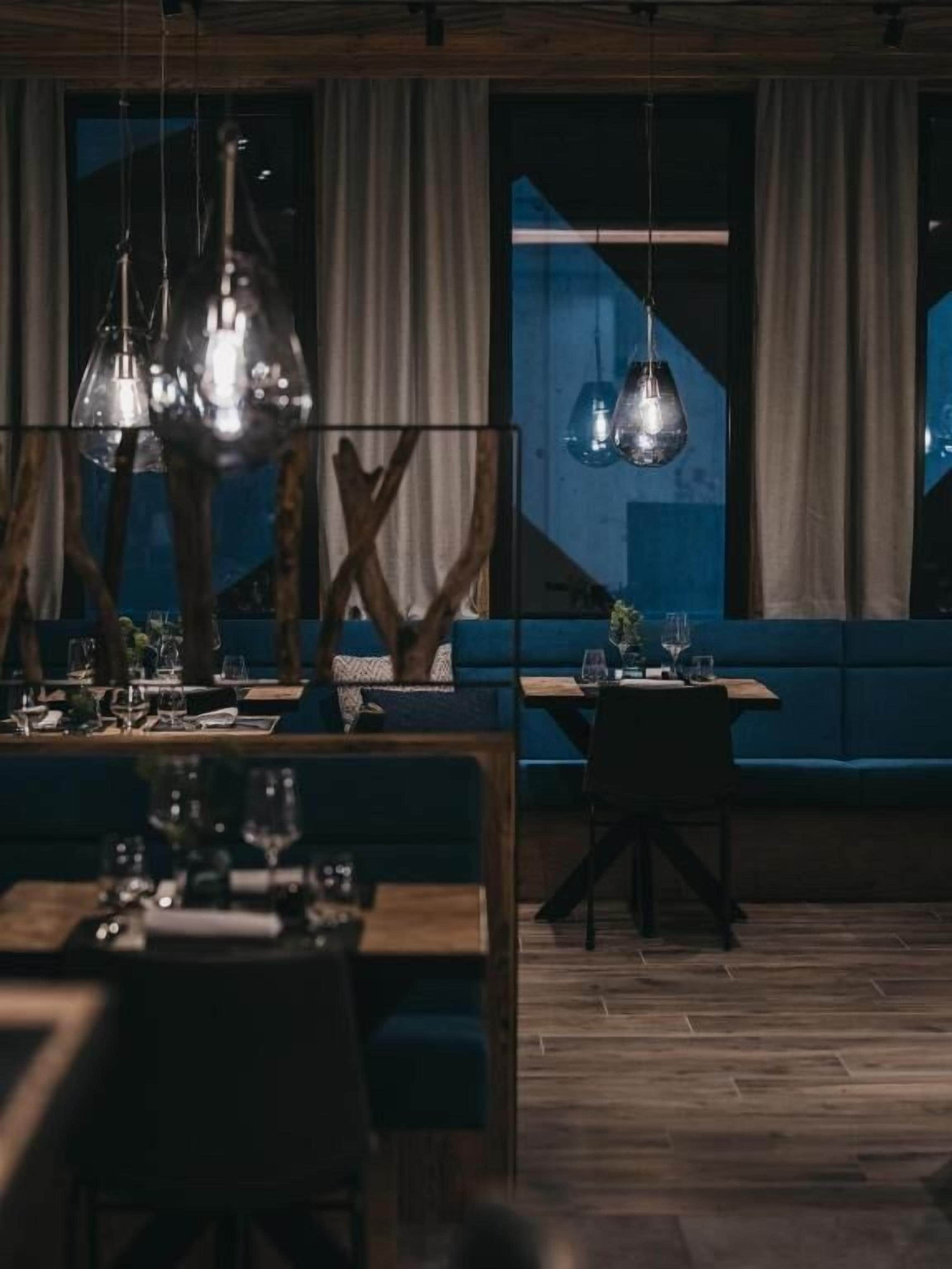 A dimly lit restaurant with wooden furniture, hanging pendant lights, and a blue cushioned bench.