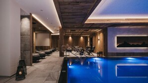 A modern indoor swimming pool with a wooden ceiling and a lounge area with seating and a painting on the wall. - VAYA Ladis (Ladis)