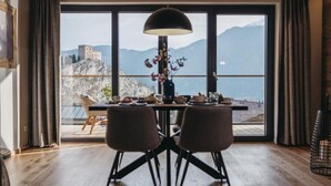 A dining area with a table set for two, a pendant light, and a view of a mountainous landscape through large windows. - VAYA Ladis (Ladis)