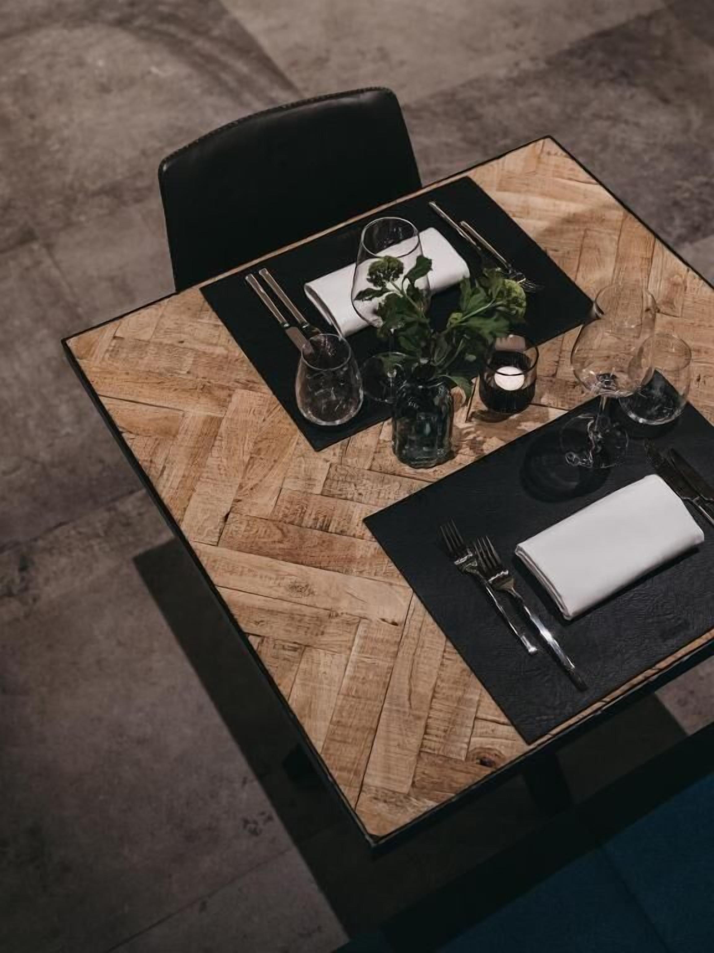 Una mesa de comedor con superficie de madera, caminos de mesa negros y servilleta blanca.