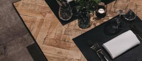 Una mesa de comedor con superficie de madera, caminos de mesa negros y servilleta blanca.