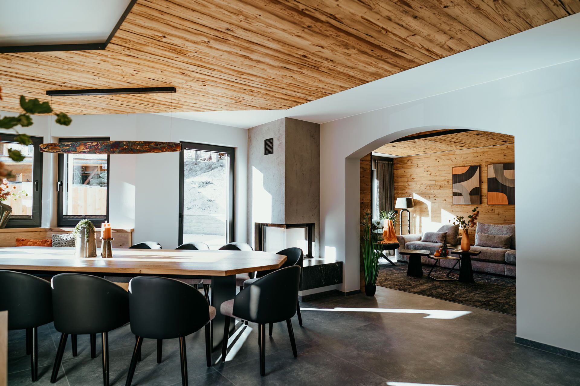 A modern interior with a wooden ceiling, a dining area with a table and chairs, and a living space with a sofa and plants.