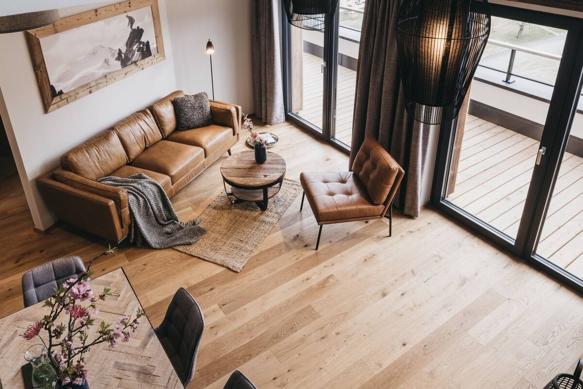 A modern living room with a leather sofa, a wooden coffee table, a leather armchair, and a large window offering a view of the outdoors.